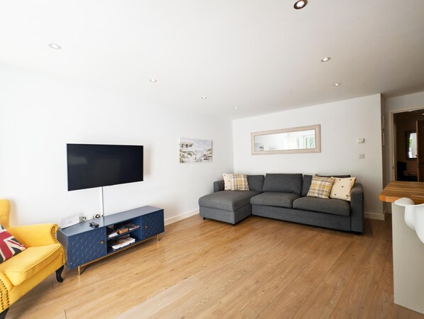 A modern living room with a flat-screen TV, a grey sectional sofa, a yellow armchair, and a blue console table.