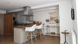 A modern kitchen with a central island, white bar stools, a hanging light fixture, and a framed artwork on the wall. - Newquay Escape/10 min to Beach/patio/parking (Newquay)
