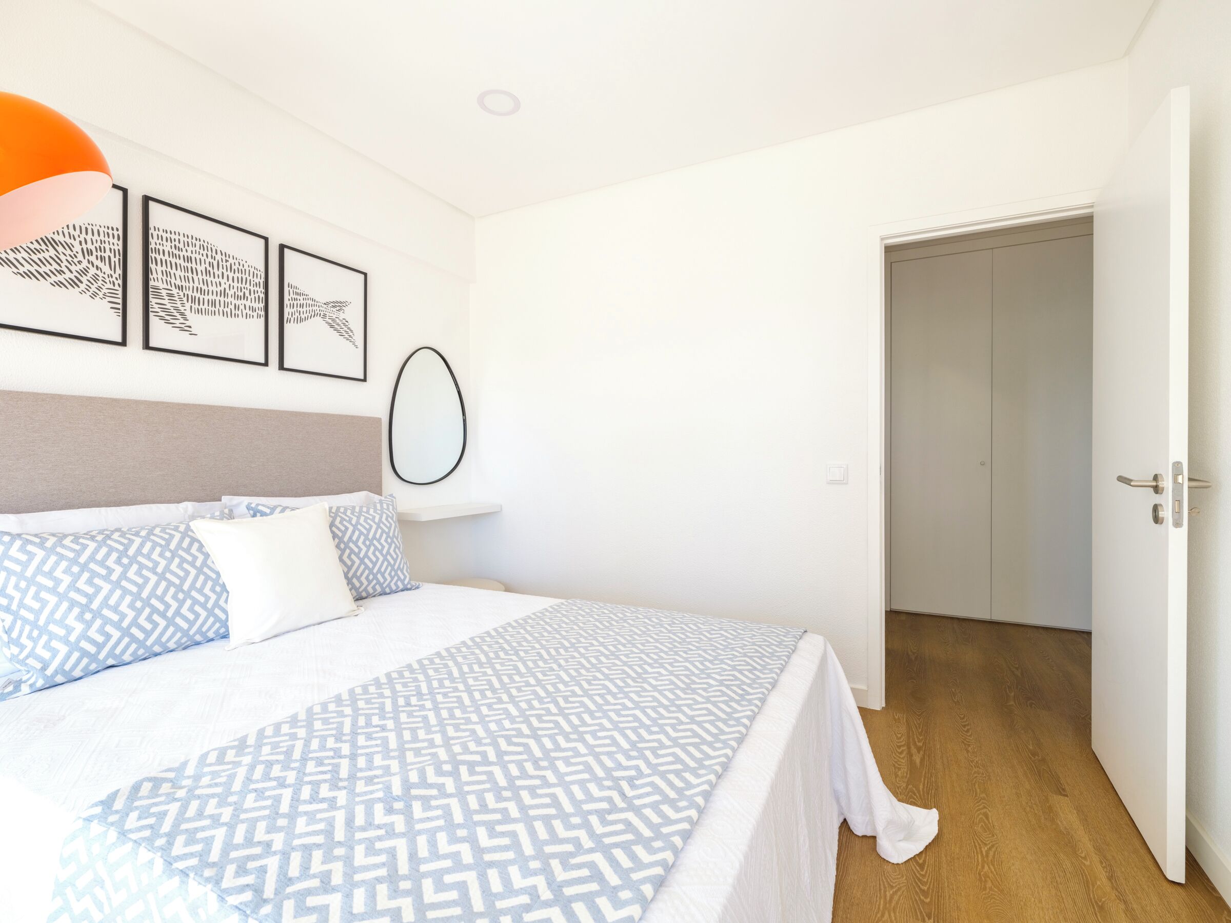 Une chambre à coucher comprenant un lit, une tête de lit, une étagère fixée au mur et une porte.