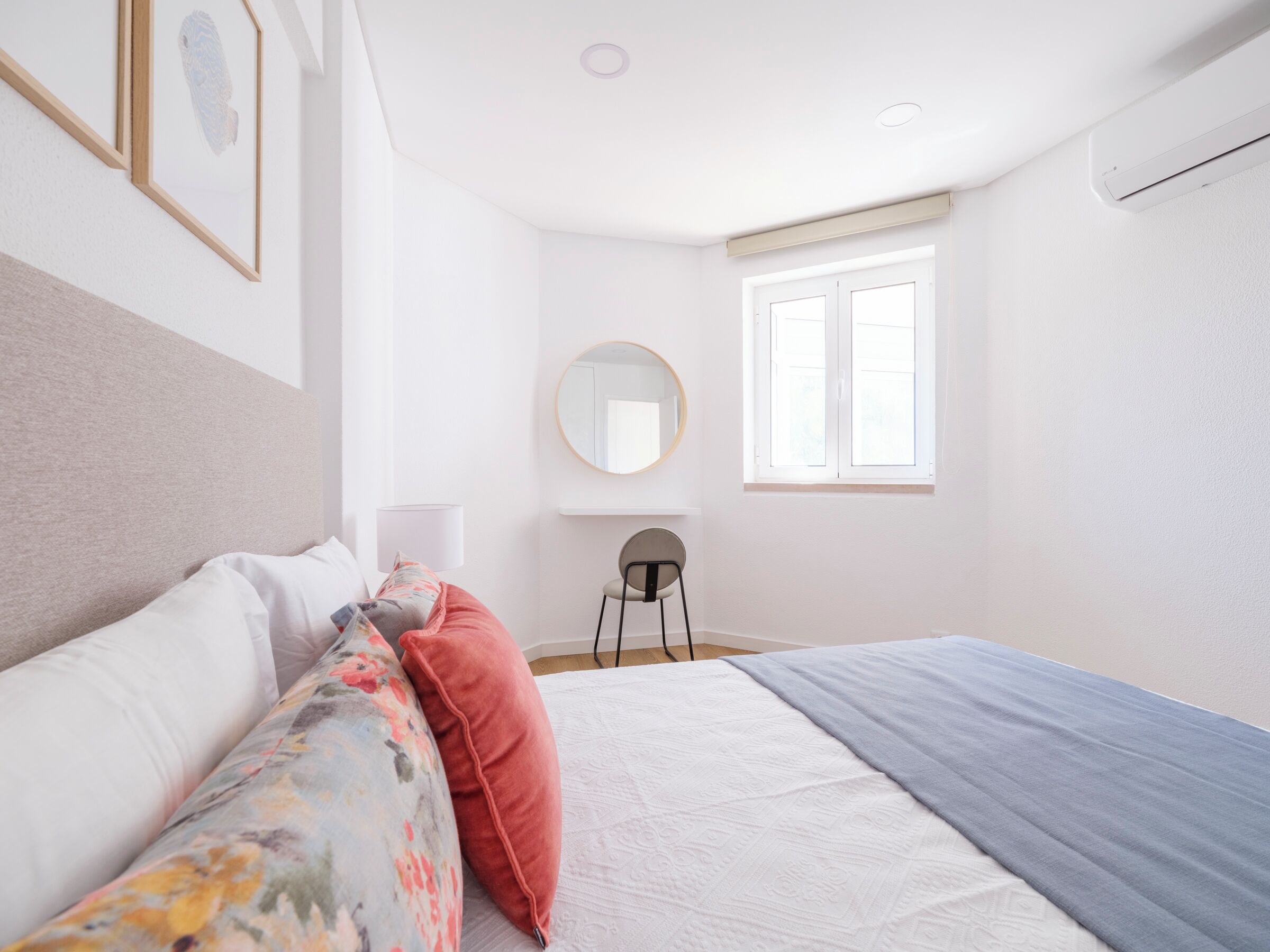 A bedroom with a bed, a chair, a round mirror, and a window.