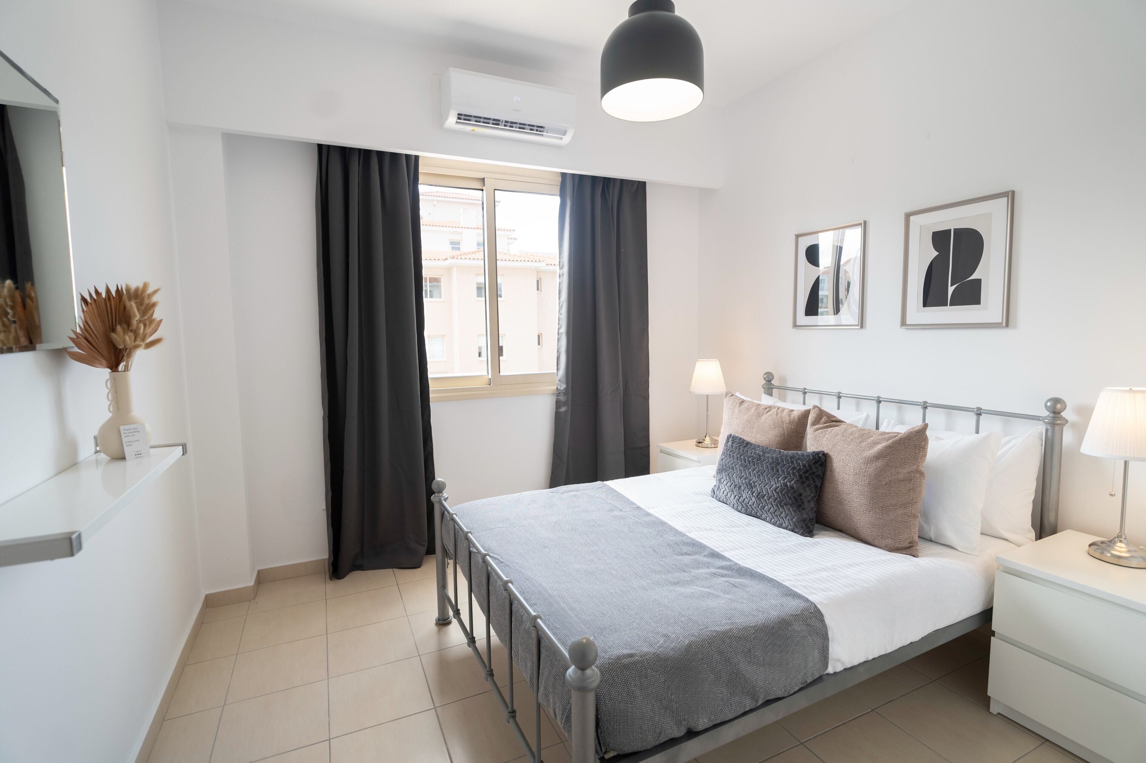 Un dormitorio moderno con cama, mesitas de noche, lámpara y ventana con cortinas.