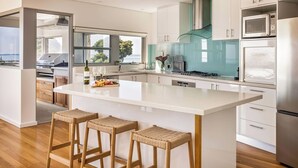 Een moderne keuken met een groot eiland, barstoelen, roestvrijstalen apparatuur en uitzicht op buiten.