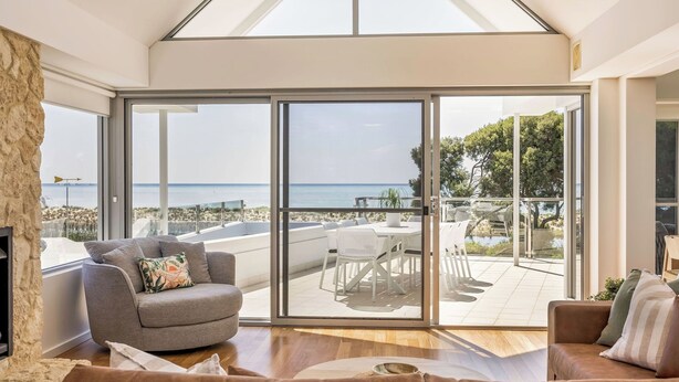Een moderne woonkamer met een grote schuifpui die uitkomt op een terras met uitzicht op zee.