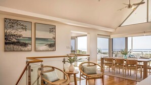 Een modern interieur met een houten eethoek, rieten stoelen en kunstwerken met kustlandschappen.