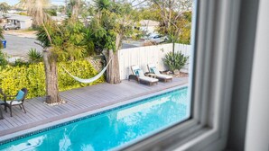 A swimming pool with lounge chairs and a hammock, surrounded by tropical plants and a white fence. - Tranquil Escape Pool Hot Tub Game Room (San Diego)