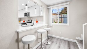 A modern kitchen with white cabinets, a stainless steel sink, and a window with a view of the outside. - Tranquil Escape Pool Hot Tub Game Room (San Diego)