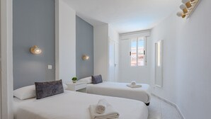 A hotel room with two beds, a small table, a plant, and a window.