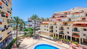 A hotel with multiple balconies, a swimming pool, and palm trees.