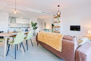 En moderne stue med sofa, spisebord, stole og et køkken i baggrunden.