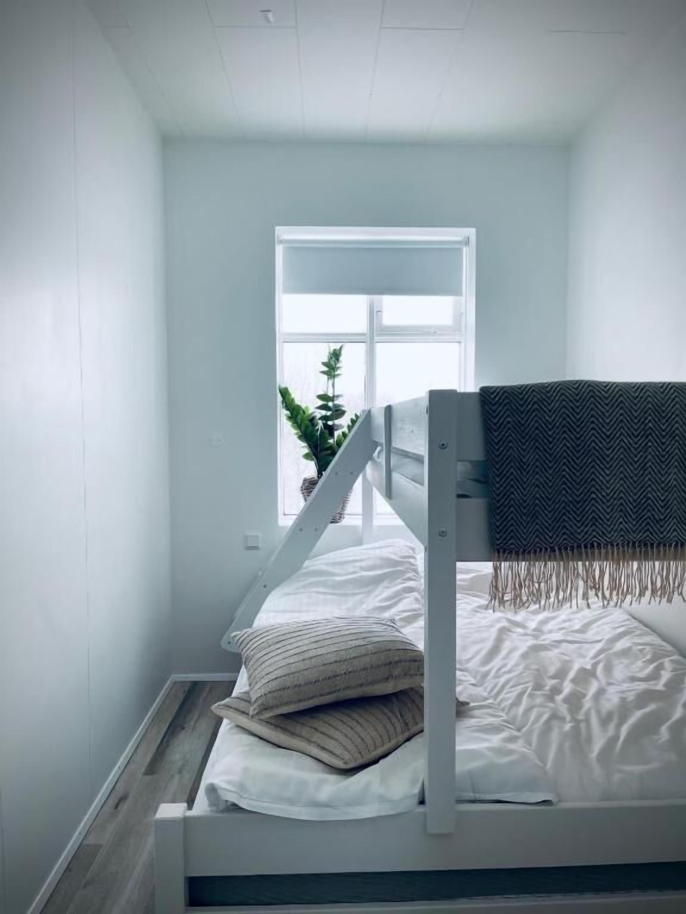 A bunk bed with a white frame, a striped pillow, and a blanket. There is a window with a view of a plant outside.