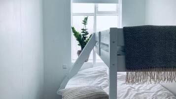 A bunk bed with a white frame, a striped pillow, and a blanket. There is a window with a view of a plant outside.