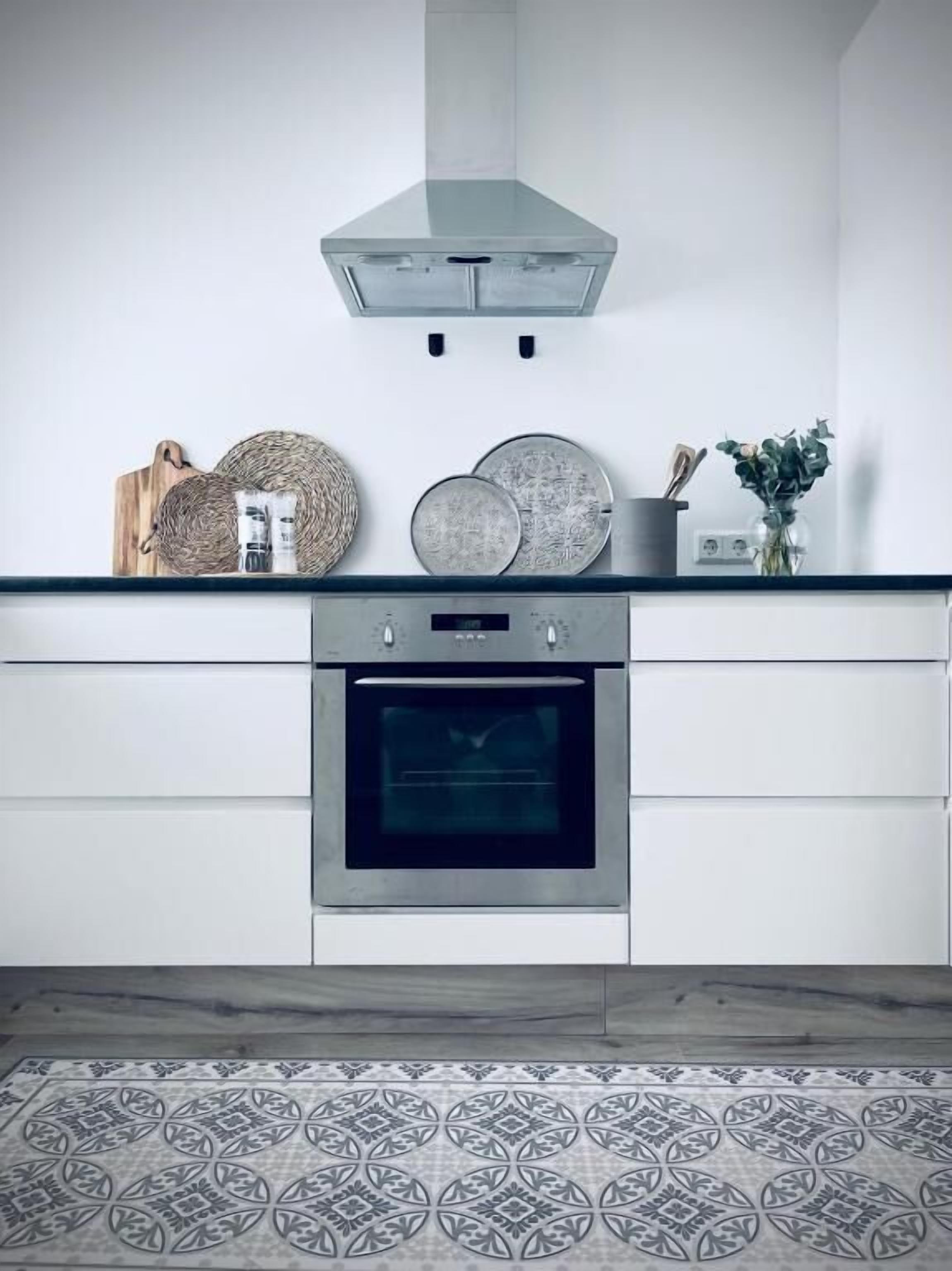 Eine moderne Küche mit Edelstahlbackofen, Glaskuppenlüfter und einem fugenlosen Boden mit Musterfliesen.