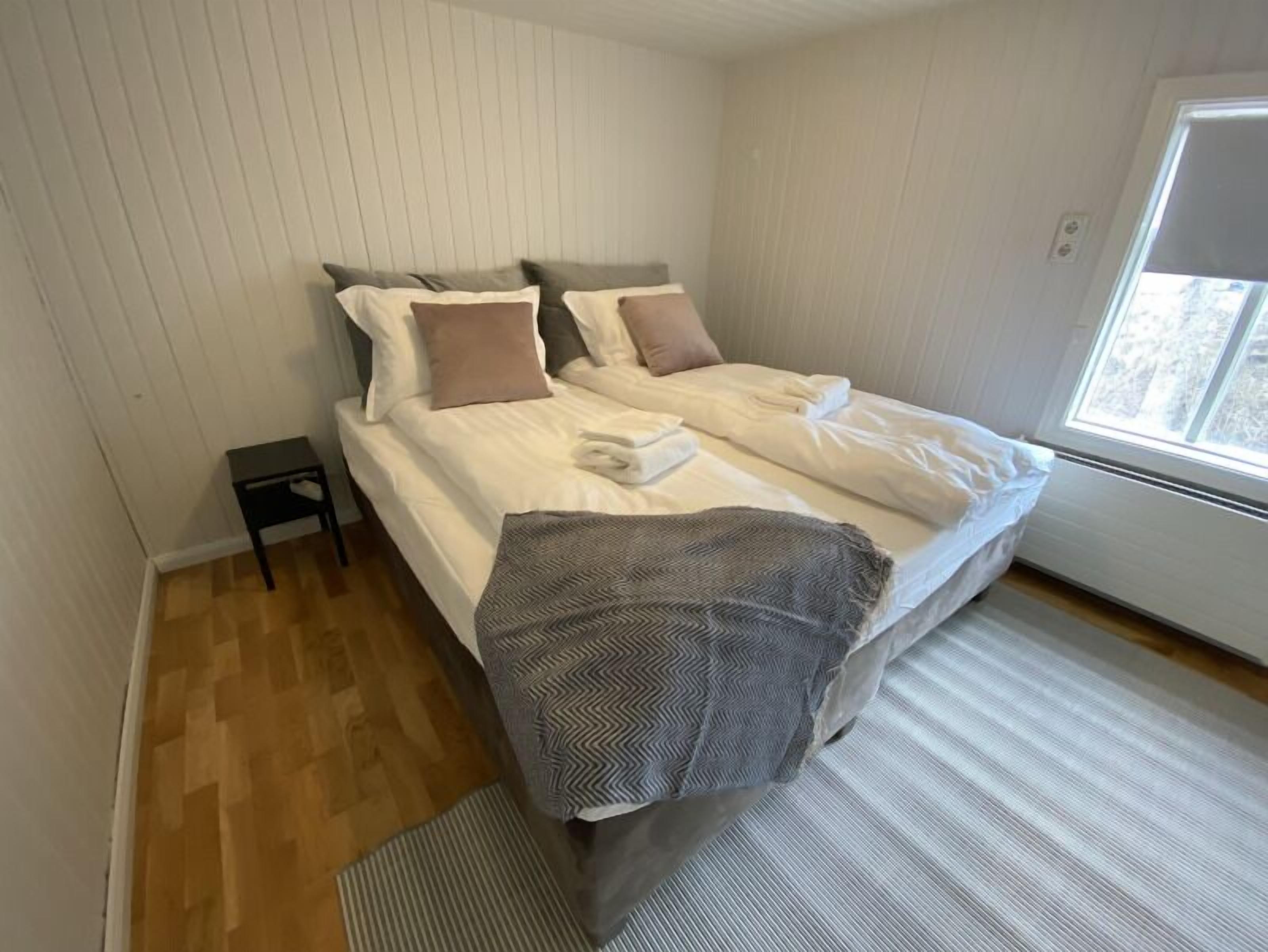 A bedroom with a bed, pillows, a small table, and a window.