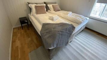 A bedroom with a bed, pillows, a small table, and a window.