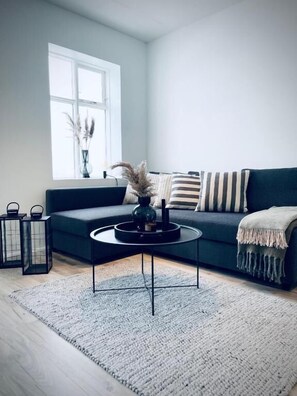 Una sala de estar moderna con un sofá oscuro, una mesa de centro redonda y un ventanal grande.