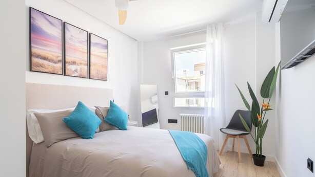 A bedroom with a bed, a desk, a chair, and a window.