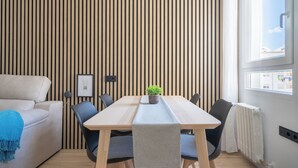 A modern room with a wooden slat wall, a sofa, a dining table with chairs, a potted plant, and a window with a view.