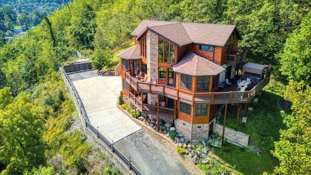 A large, multi-story log cabin with a wrap-around deck, situated in a lush, mountainous area.