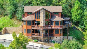 A multi-story log cabin with a stone foundation, multiple balconies, and a stone retaining wall.