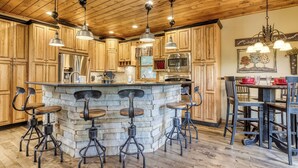 A kitchen with wooden cabinets, a central island with stools, stainless steel appliances, and pendant lighting.