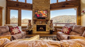 A cozy living room with a fireplace, two couches, and a large TV screen.