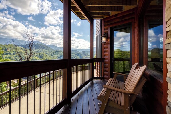 Una terraza de madera con sillas Adirondack, un muro de piedra y vistas a un paisaje montañoso.