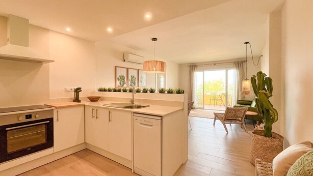 A modern kitchen with white cabinets, a built-in oven, and a dishwasher. There is a dining area with a table and chairs, and a large cactus plant. - Miramar Apartment (Denia)