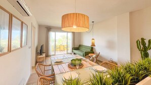 A modern living room with a dining area, a green sofa, wicker chairs, and a table set for a meal. - Miramar Apartment (Denia)