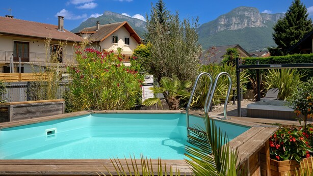 Una piscina con cubierta de madera, rodeada de abundante vegetación y con montañas al fondo.