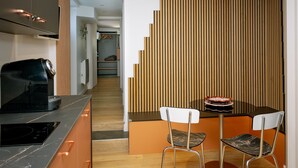 Una cocina moderna con estufa integrada, comedor con mesa y sillas, y pared de paneles de madera vertical.