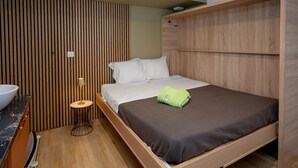Una habitación moderna con cama, una mesita redonda con lámpara y un panel de pared de madera.