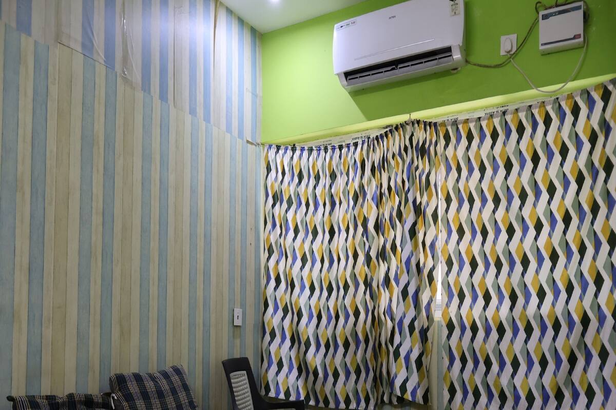 Et soveværelse med en stribet væg, en seng med blomstret sengetæppe, en stol og en aircondition.