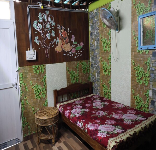 A bedroom with a bed, a wall-mounted fan, a decorative tree mural, and a wicker stool. - Saikani Beach Resort and EcoStay (Puducherry)