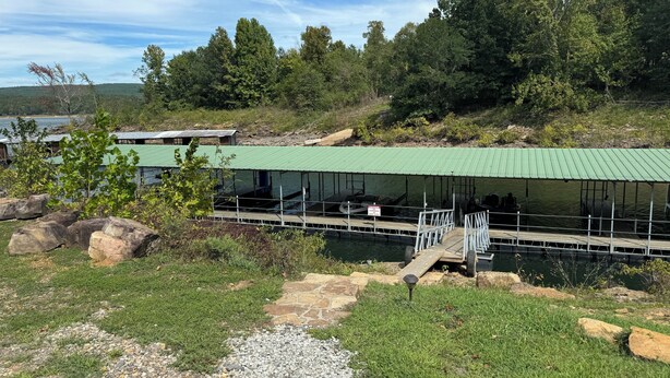 A dock with a covered boat ramp, a small building with a green roof, and a natural landscape with trees and a body of water. - Bellawood Resort #5 - Lake Cabin with boat slip (Greers Ferry)