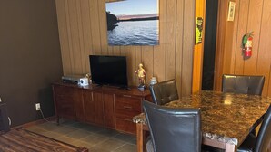 A dining area with a marble table and chairs, a television on a wooden cabinet, and a painting on the wall. - Bellawood Resort #5 - Lake Cabin with boat slip (Greers Ferry)