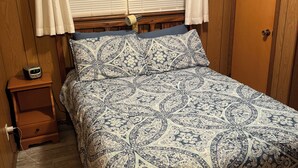 A bedroom with a wooden headboard, a bed with a patterned bedspread, a bedside table with a clock, and a wooden wardrobe. - Bellawood Resort #5 - Lake Cabin with boat slip (Greers Ferry)