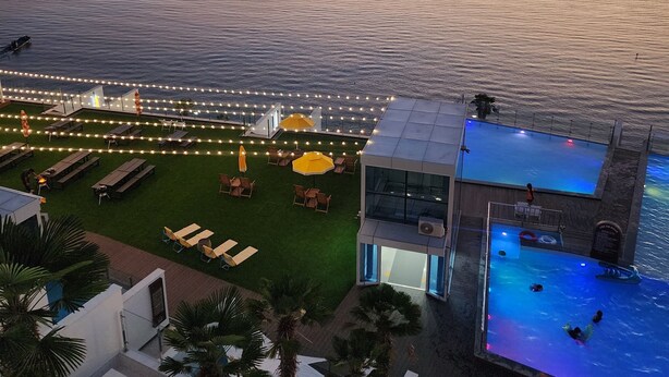 A resort with a pool, outdoor seating, and a view of the sea at sunset.
