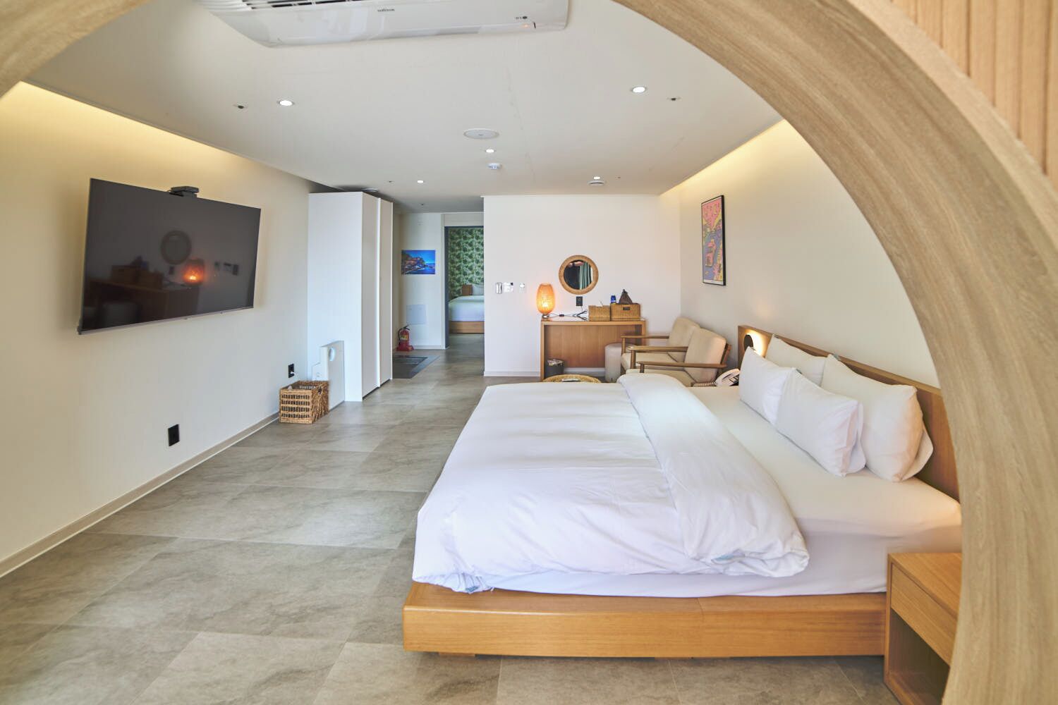 Una habitación de hotel moderna con una cama grande, un escritorio con lámpara, un televisor montado en la pared y un arco de madera.