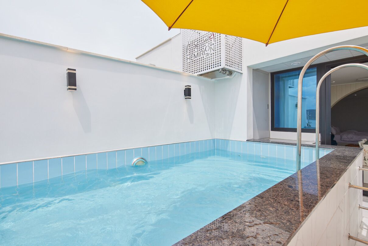 A modern indoor swimming pool with a clear blue water, a yellow umbrella, and a glass balustrade.