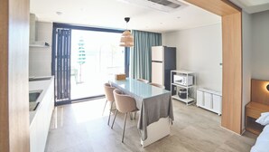 A modern hotel room with a dining area, a kitchenette, and a large window with curtains.