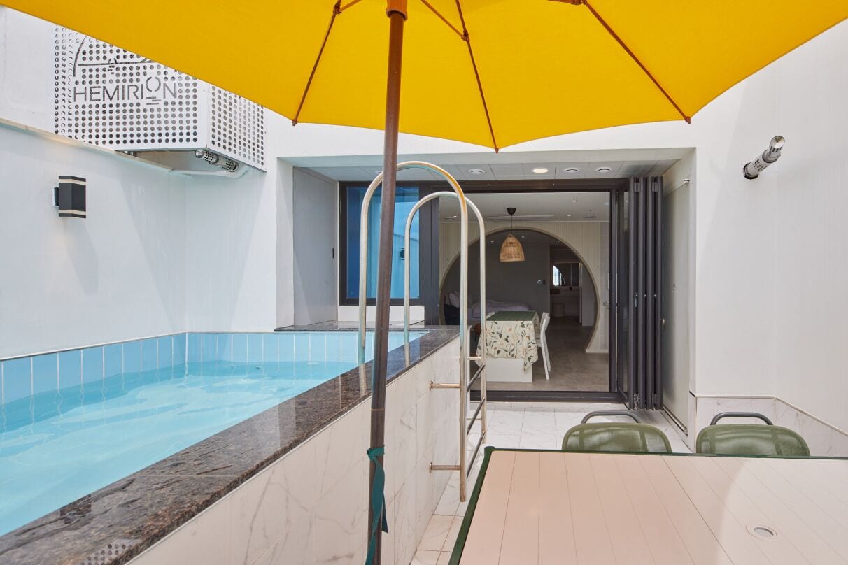 A modern hotel room with a pool, a yellow umbrella, and a view of the interior.