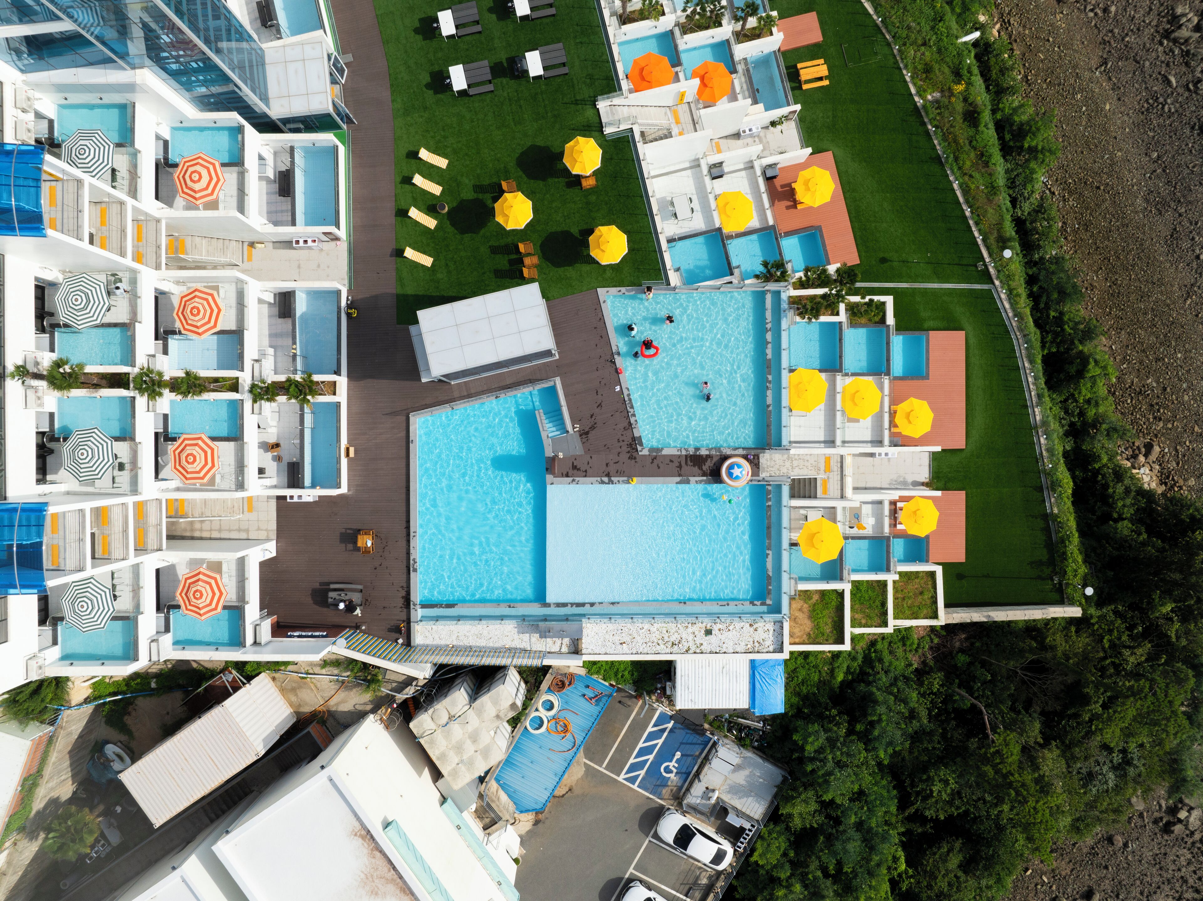 An aerial view of a hotel with multiple swimming pools, outdoor seating areas, and a parking lot.