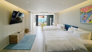 A hotel room with two beds, a TV mounted on the wall, a blue rug, and a painting on the wall.