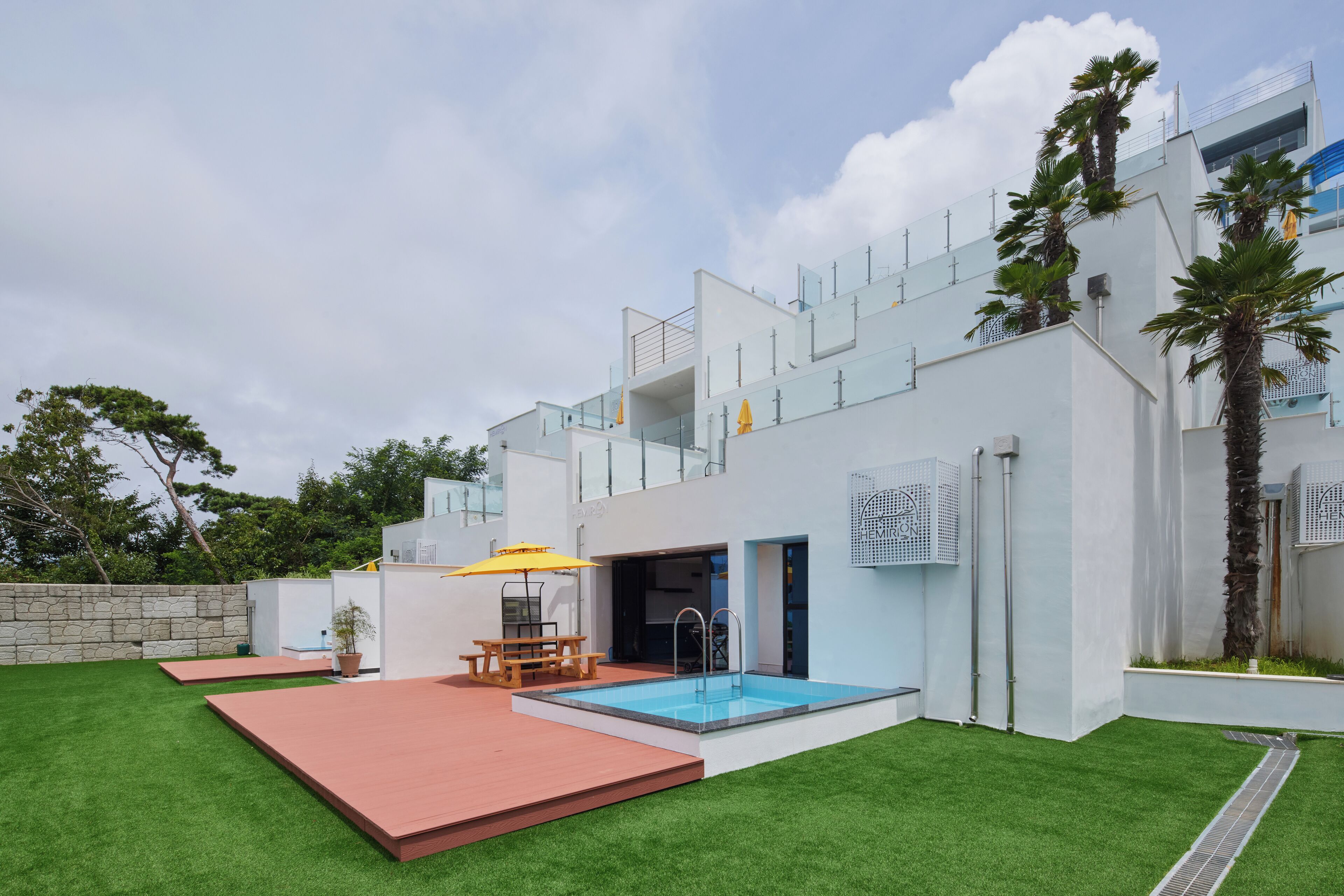A modern house with a swimming pool, a patio with a table and chairs, and a stone wall.