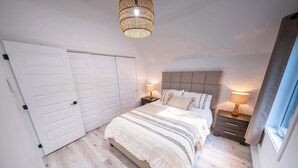 Ein Schlafzimmer mit einem großen Bett, zwei Nachttischen, einer Pendelleuchte und einem Fenster mit Vorhängen.