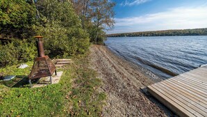 A lakeside deck with a rustic metal structure, a wooden platform, and a shoreline with trees and a clear sky. - SPA - Lake - Foosball Table | Chalet le Relaxarium (Lac-Etchemin)