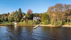 A lakeside property with a dock extending into the water, surrounded by trees and a house with a balcony. - SPA - Lake - Foosball Table | Chalet le Relaxarium (Lac-Etchemin)