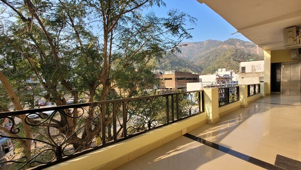 A balcony with a view of trees and buildings, a tiled floor, and a metal railing.