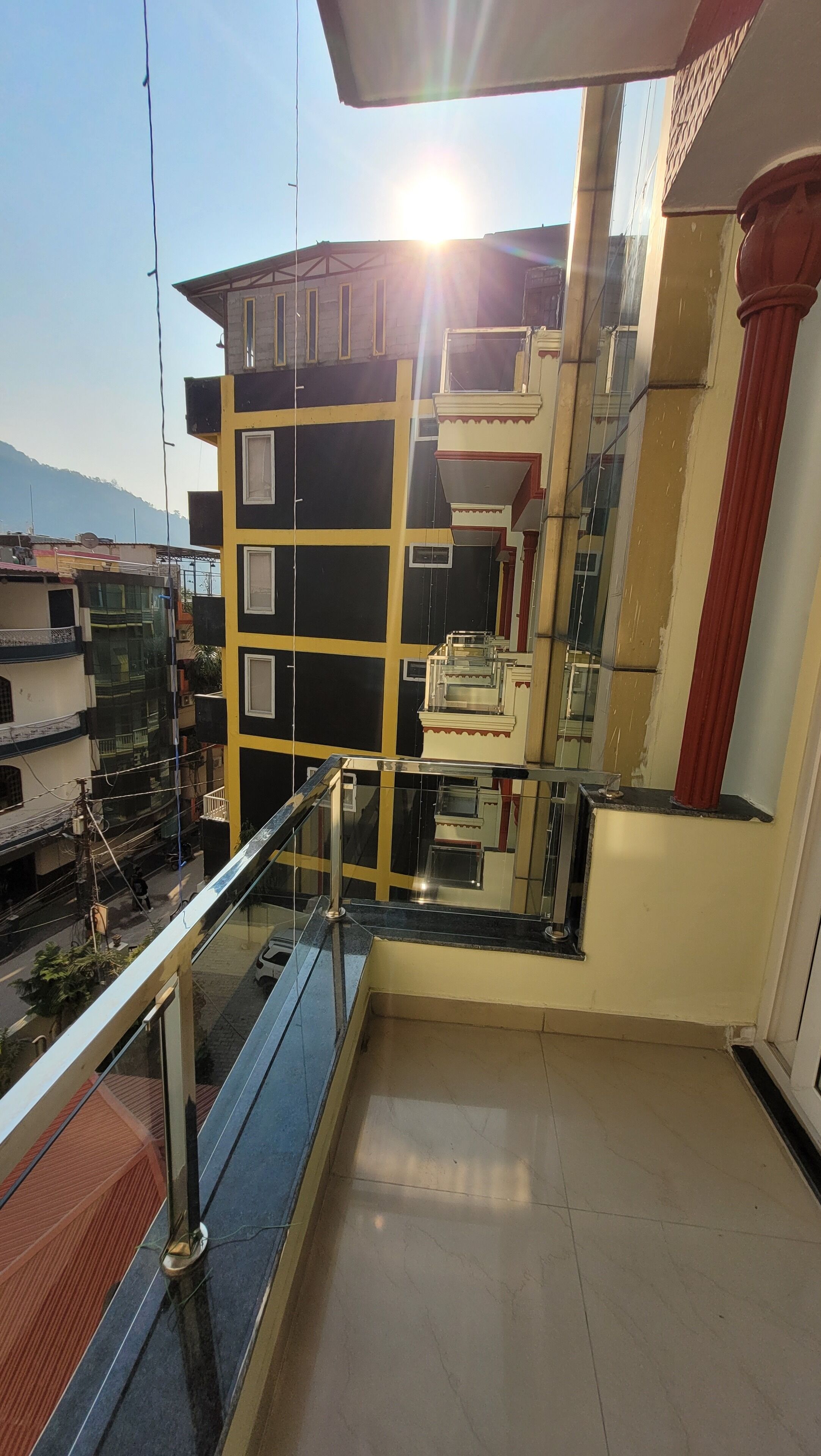 A balcony with a glass railing overlooking a building with multiple floors and a red column.