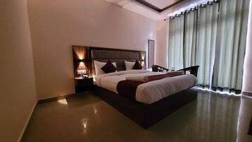A hotel room with a large bed, a nightstand with a lamp, and a view of the outside through curtains.